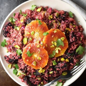 Top down view of quinoa and beet salad with 3 orange slices on top on pink plate.