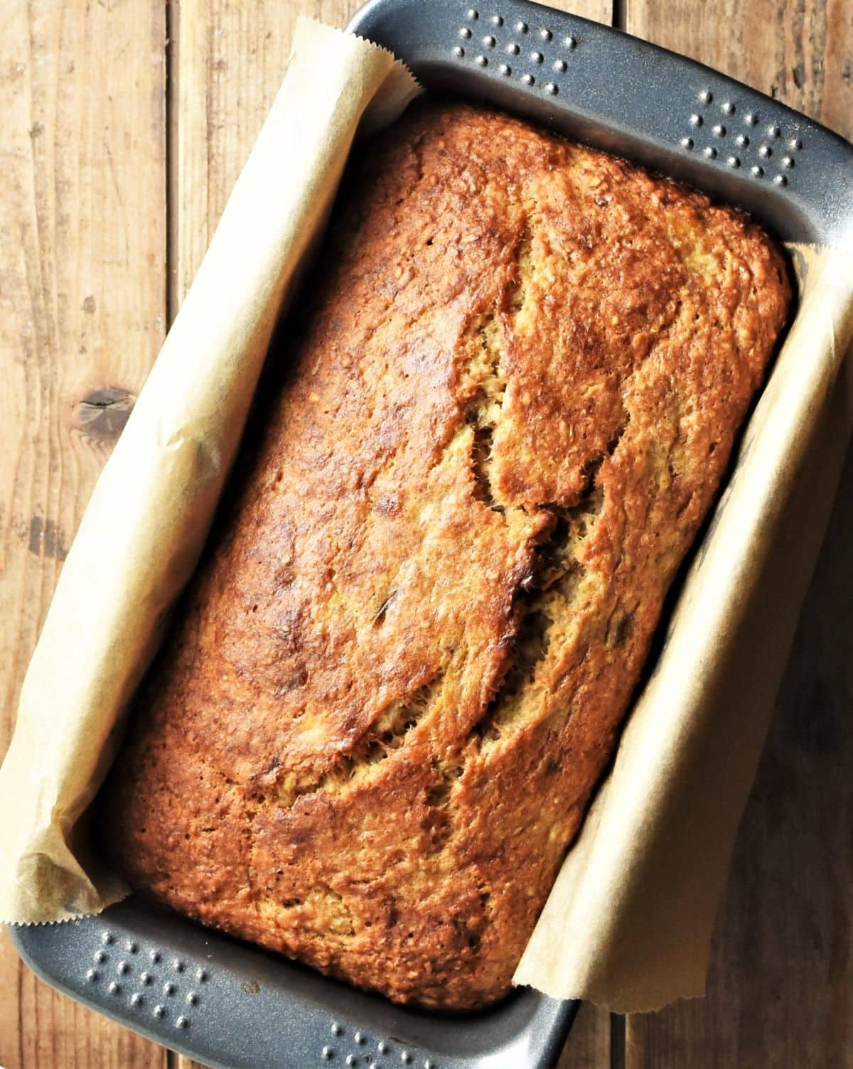 Top down view of banana bread in pan lined with paper.