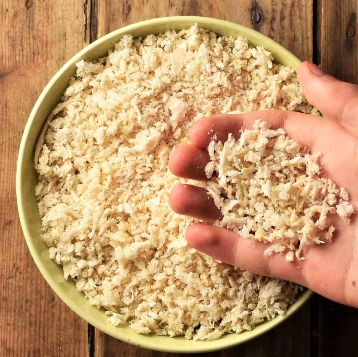 Hand holding breadcrumbs over yellow bowl.