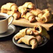Side view of Polish rogaliki crescent cookies on saucer and wooden board.