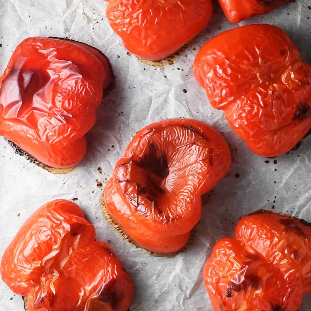 Roasted halved red peppers on top of parchment paper.