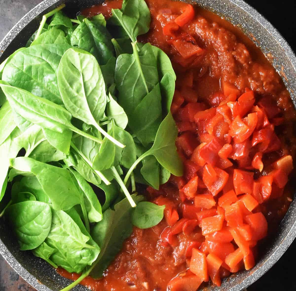 Top down view of fresh spinach with tomato red pepper sauce in pan.