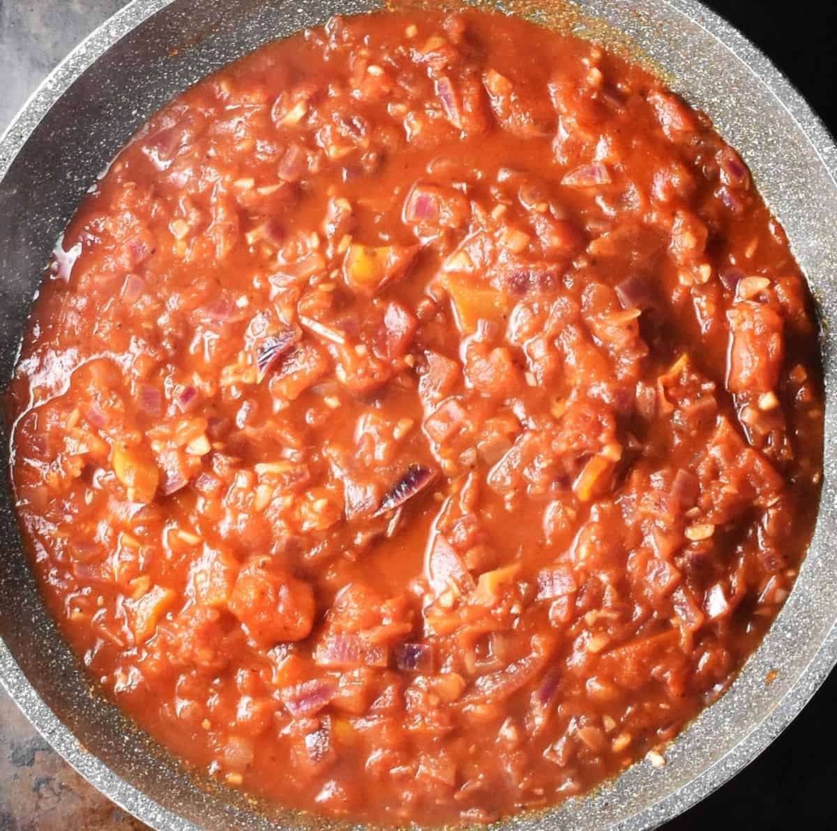 Top down view of tomato sauce with chopped red peppers in parge pan.