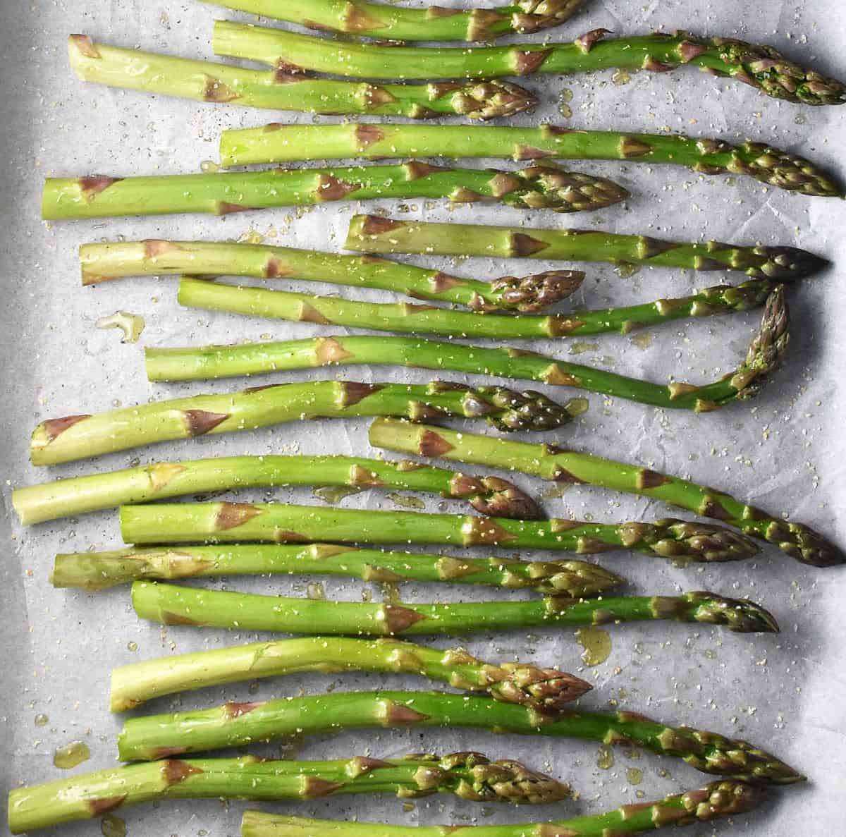 Top down view of seasoned asparagus tips on parchment.