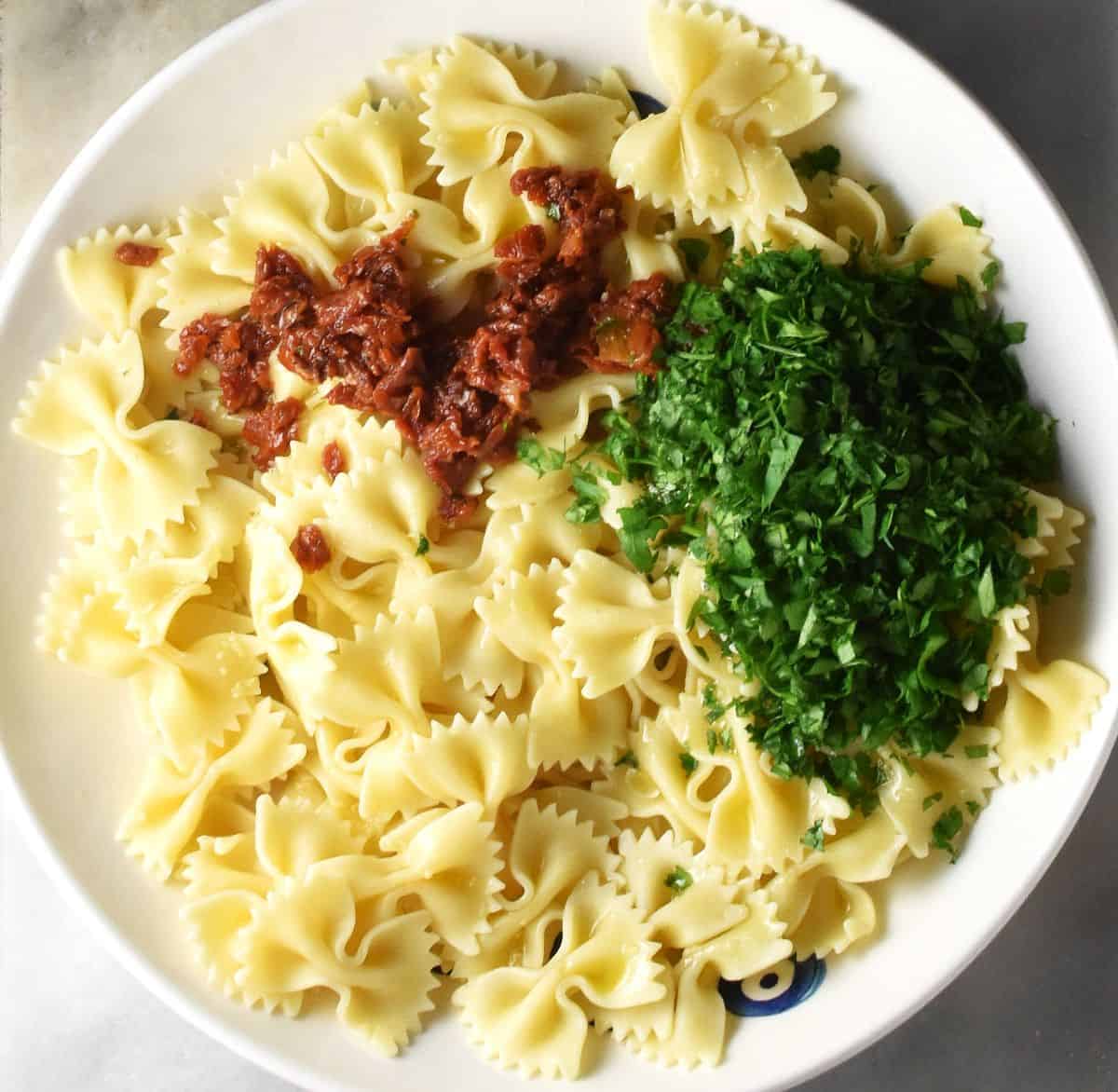 Farfalle pasta with chopped sundried tomatoes and parsley in white bowl.