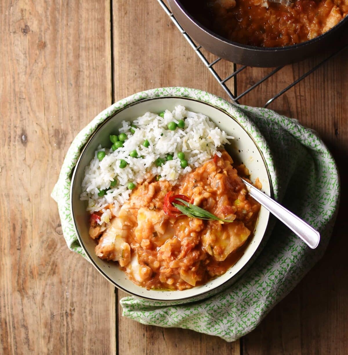 Tomato lentil fish stew with rice and spoon inside white bowl wrapped in green cloth.