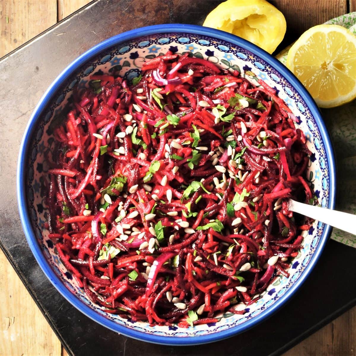 Shredded raw beet salad in large blue bowl with lemon in background.