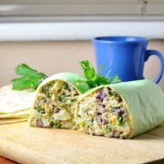 Side view of halved egg salad wrap on top of wooden board with parsley leaves and blue cup in background.