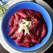 Top down view of creamy beet pasta sauce with large pasta in blue bowl.