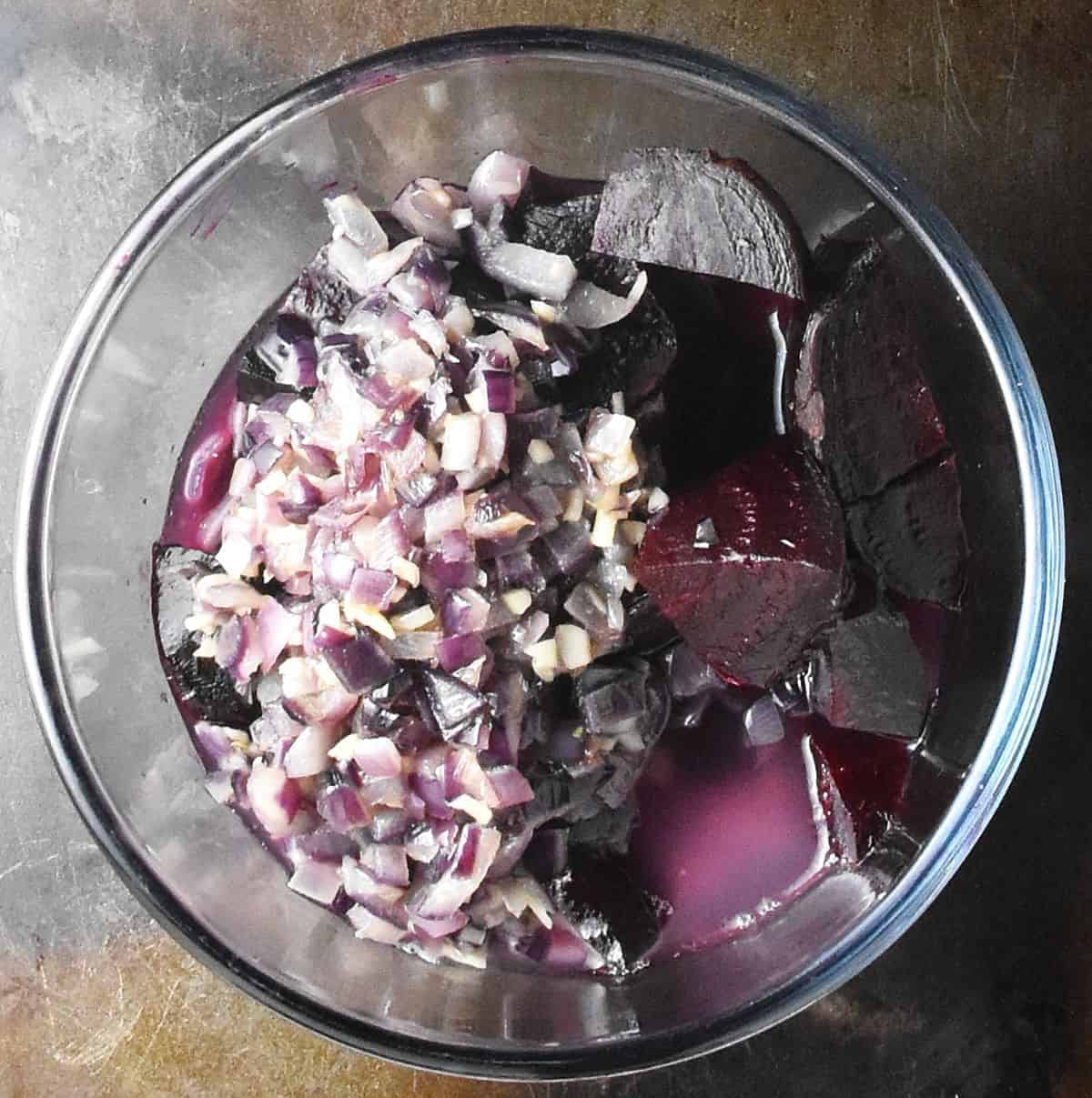 Chopped red onion, cooked beets and stock in glass bowl.