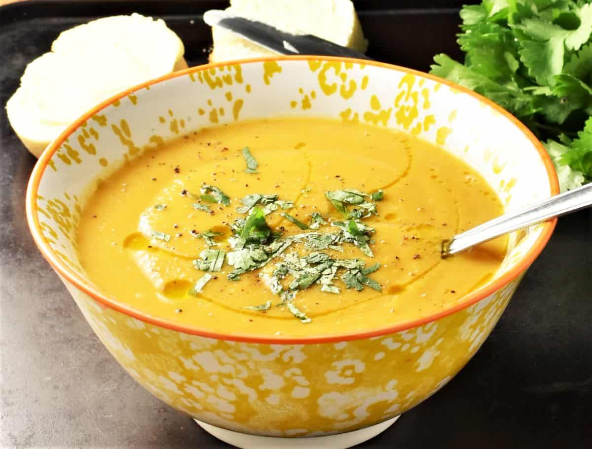 Side view of creamy lentil and butternut squash soup in yellow bowl with bread in background.