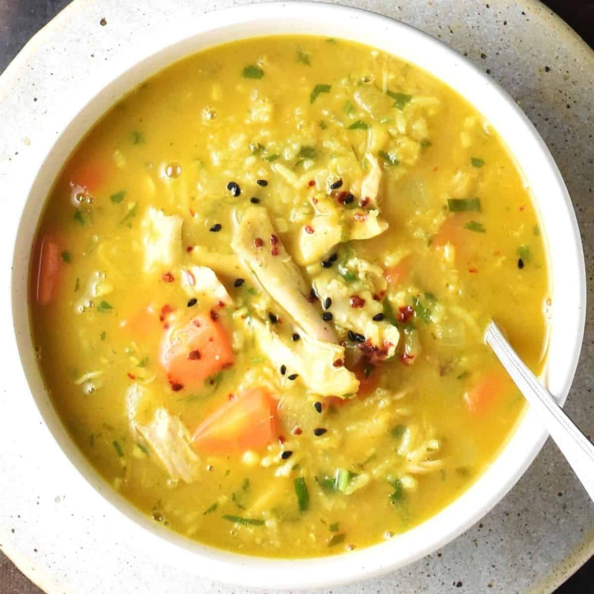 Top down view of chicken mulligatawny soup in white bowl with spoon.