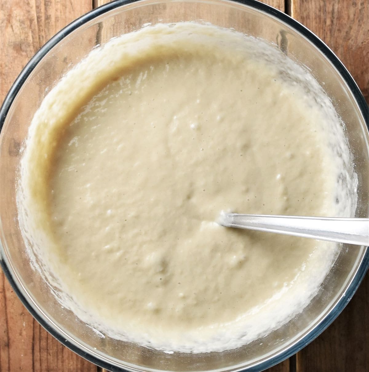 Racuchy pancakes batter in mixing bowl with spoon.