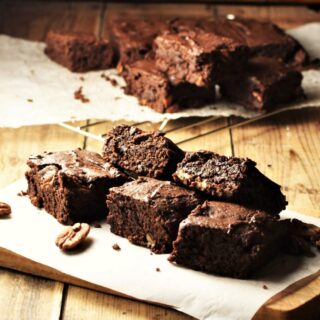 Sweet potato brownies on top of paper with pecans and brownies in background on cooling rack.