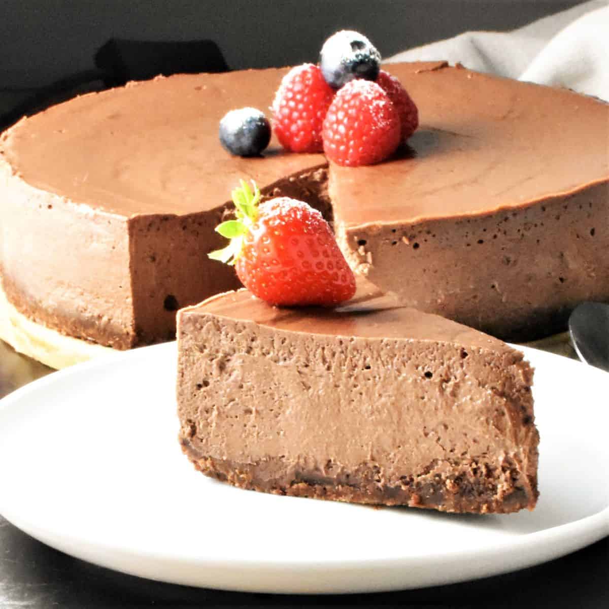 Side view of chocolate ricotta cheesecake slice on plate with cheesecake in background.