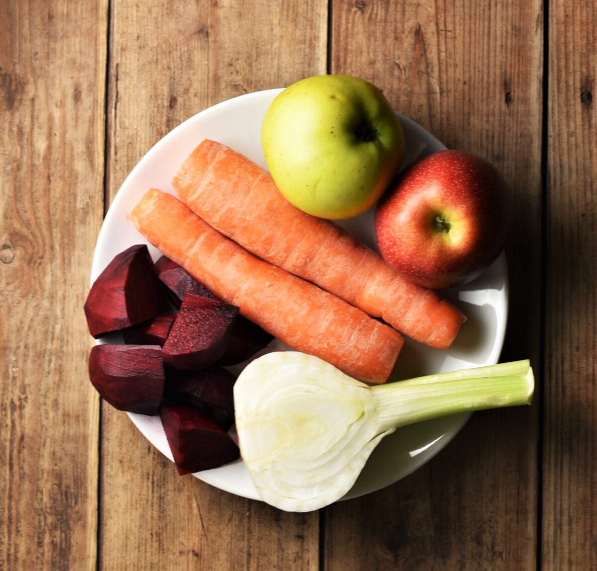 2 carrots, 2 apples, halved fennel and chopped beet on white plate.