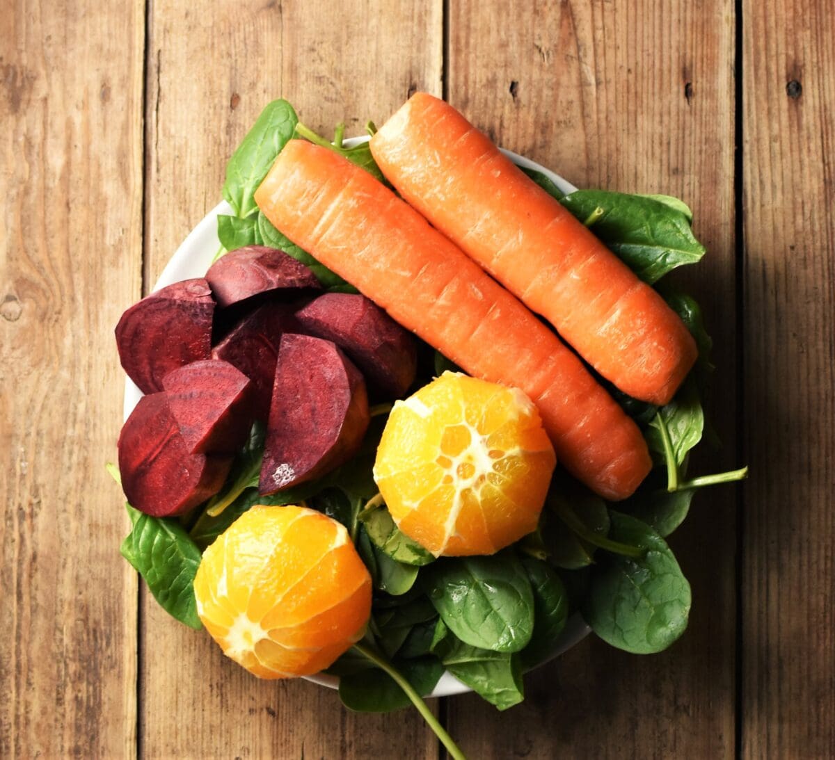 Cubed beet, 2 carrots, 2 peeled oranges on top of spinach leaves.