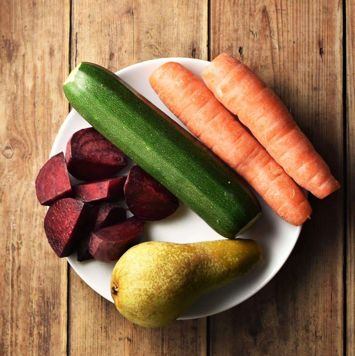 Chopped beet, zucchini, 2 carrots and pear on white plate.
