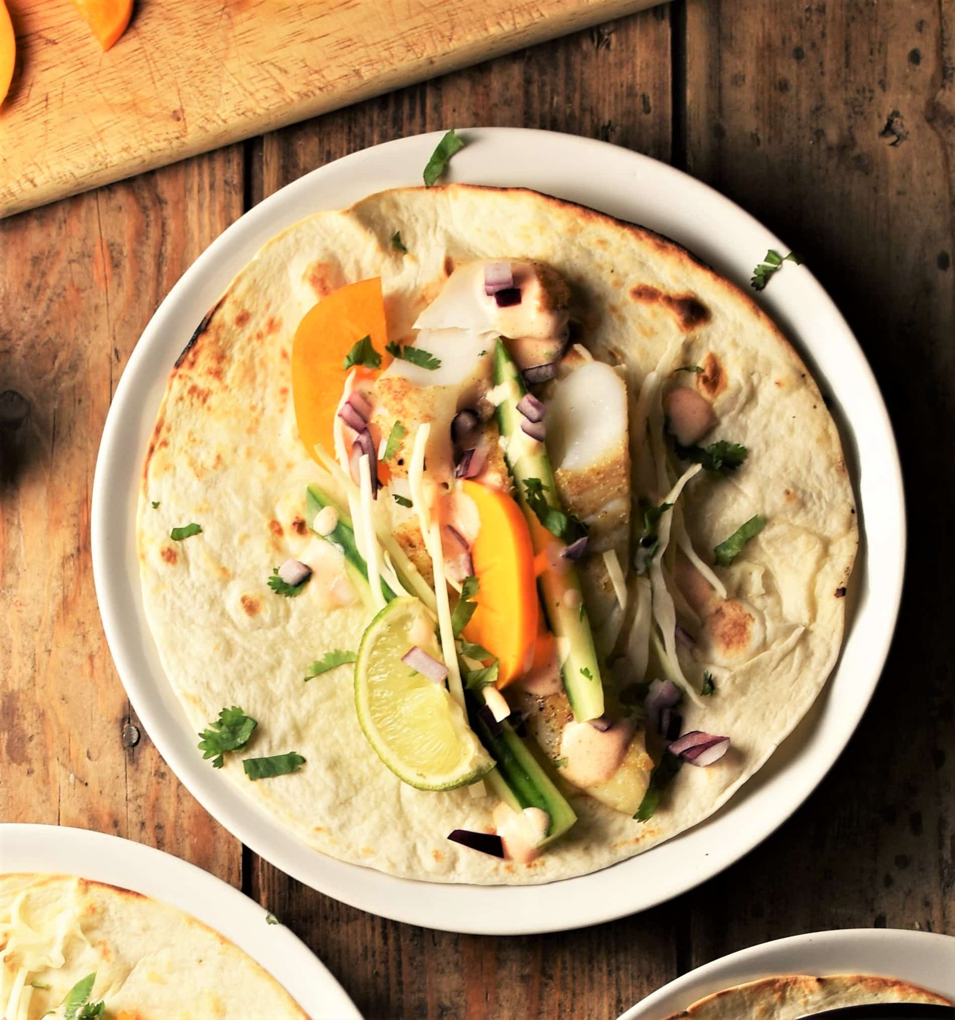 Fish taco with vegetables and fruit on top of plate.