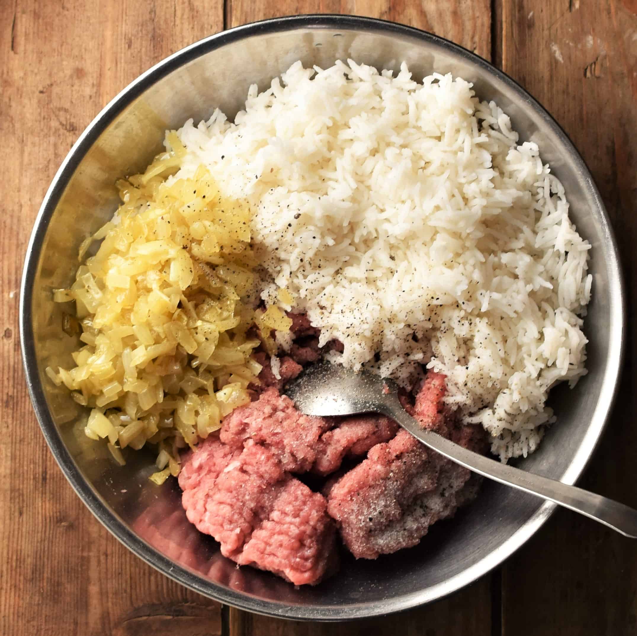 Meat, fired onion and cooked rice in metal bowl with spoon.