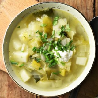Top down view of chunky leek and potato soup with yogurt and herbs in green bowl.
