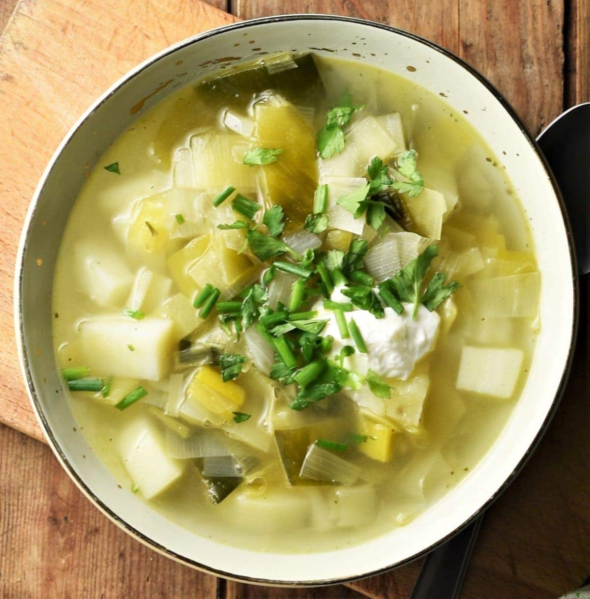Top down view of chunky leek and potato soup with yogurt and herbs in green bowl.