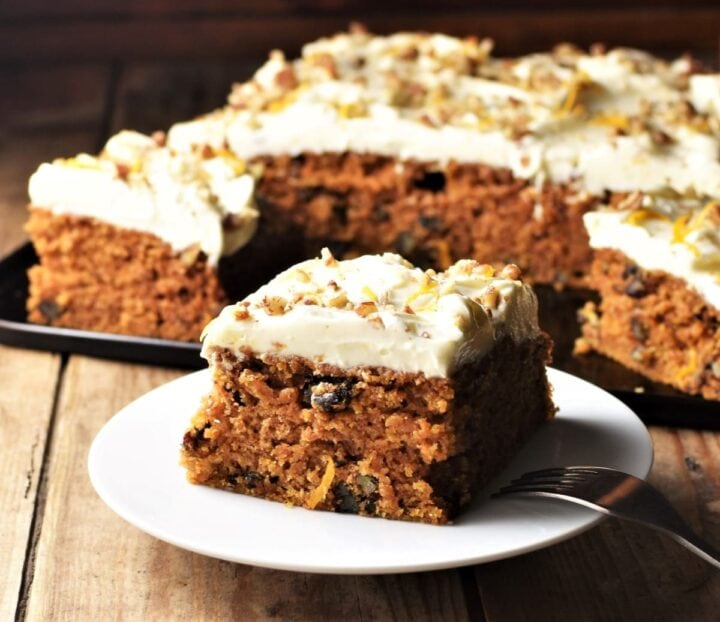 Side view of carrot cake slice on white plate with cake in background.