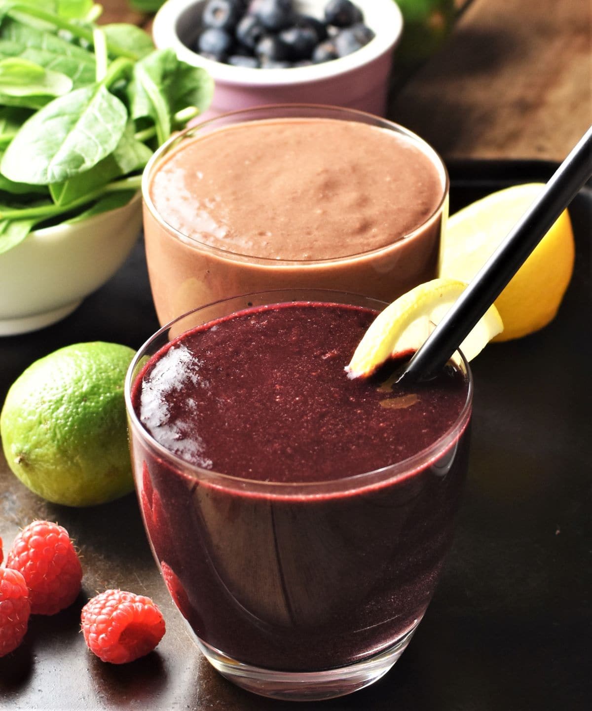 Side view of spinach berry smoothie in row with fruit and spinach in background.