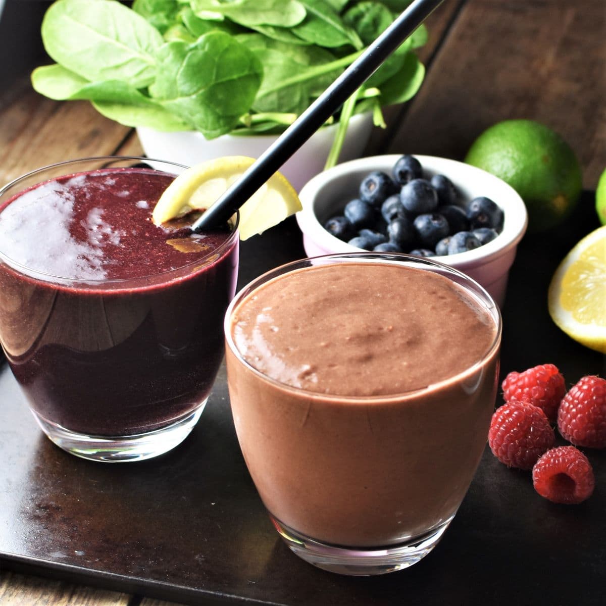 Side view of spinach berry smoothie in 2 glasses with fruit in background.