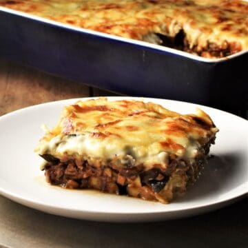 Side view of vegetarian moussaka slice on top of plate with moussaka in background.