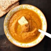 Top down view of creamy pumpkin carrot soup in yellow bowl with spoon.