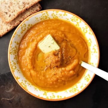Top down view of creamy pumpkin carrot soup in yellow bowl with spoon.