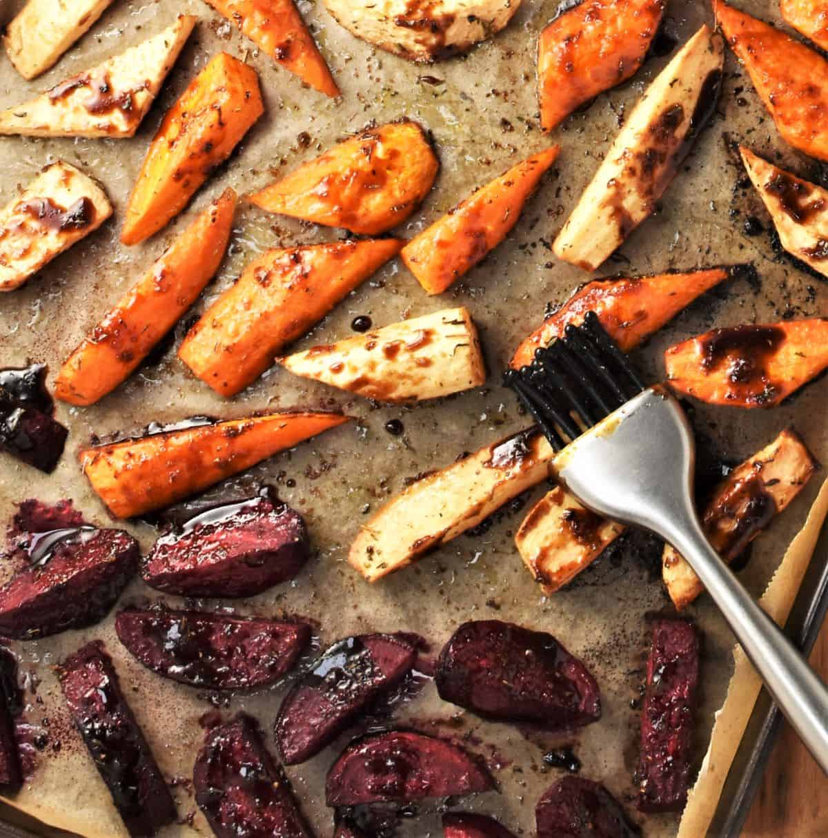 Roasted sticky vegetable pieces on parchment with pastry brush.