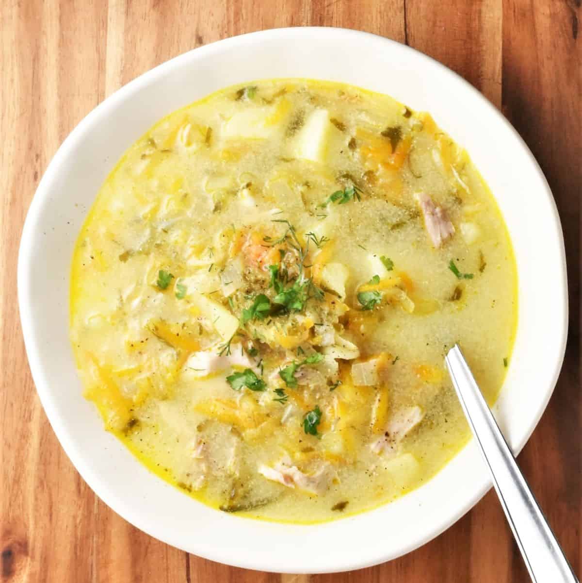 Top down view of dill pickle soup in white bowl with spoon.