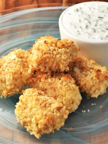 Side view of breaded fish nuggets on top of blue plate with yogurt sauce.