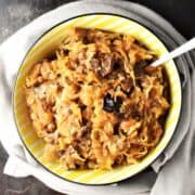 Top down view of sauerkraut with mushrooms in yellow bowl with spoon.