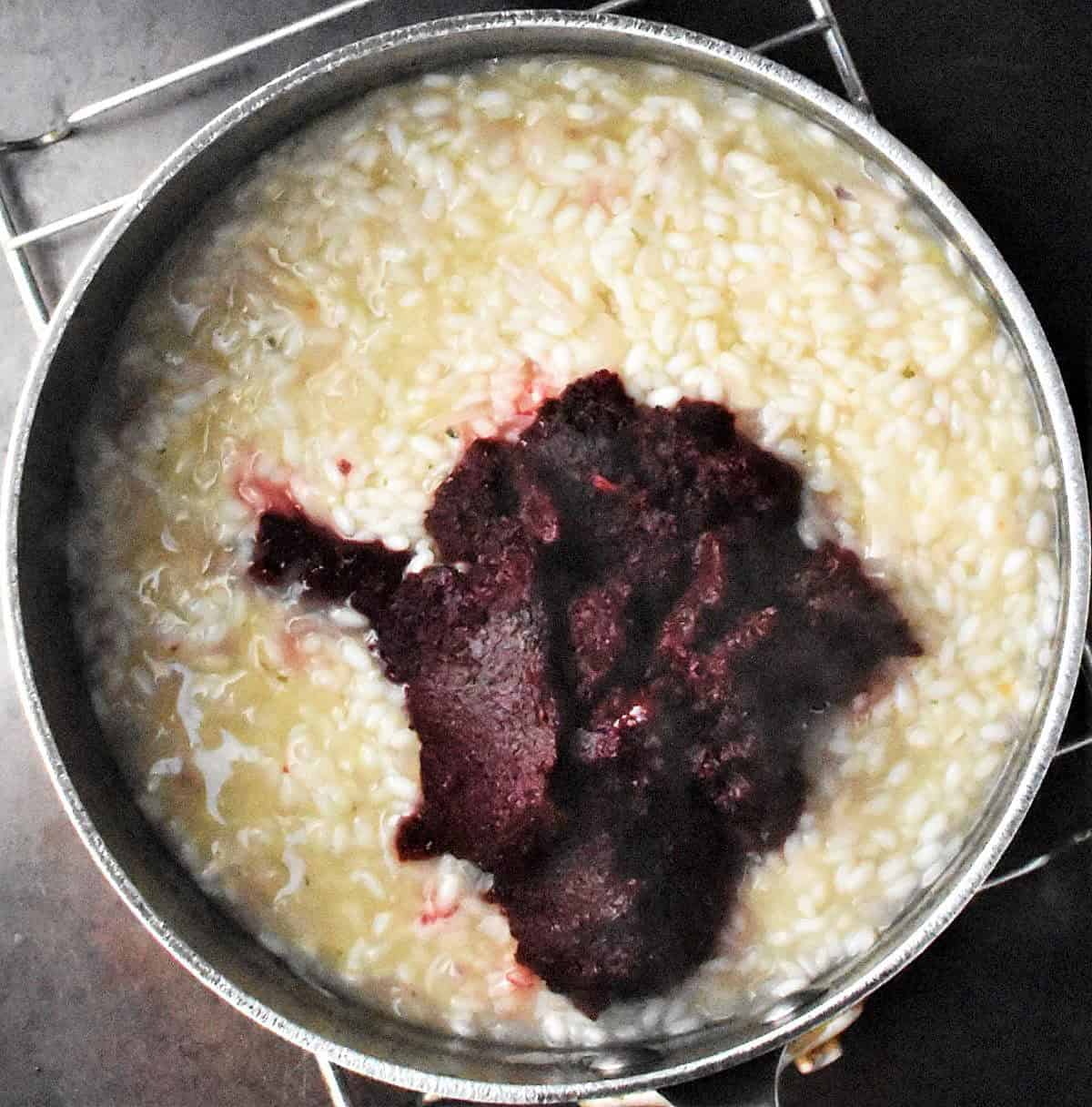 Creamy risotto with beet puree in large black pot.