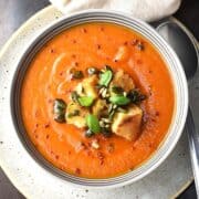 Top down view of creamy butternut squash tomato soup with croutons in grey bowl with spoon on right.