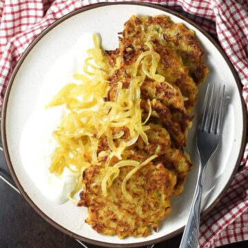 Top down view of sauerkraut pancakes with onion and sour cream on white plate.
