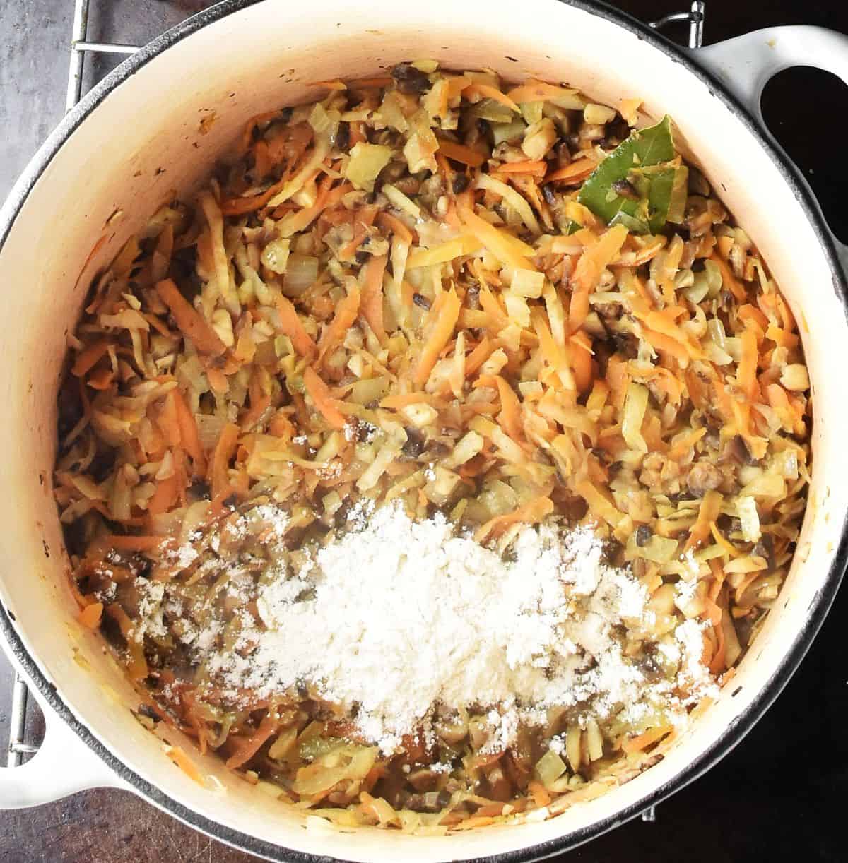 Top down view of sauteed vegetables and mushrooms and flour in large pot.