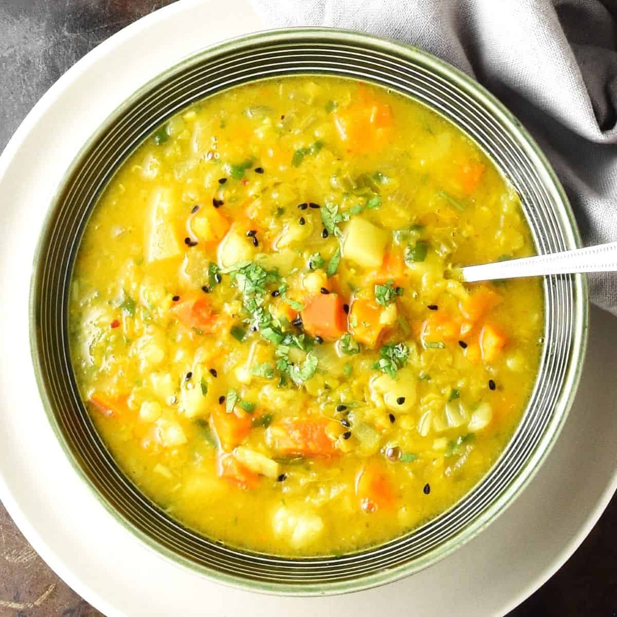 Close-up top down view of vegetable mulligatawny soup in green bowl with spoon on white plate.